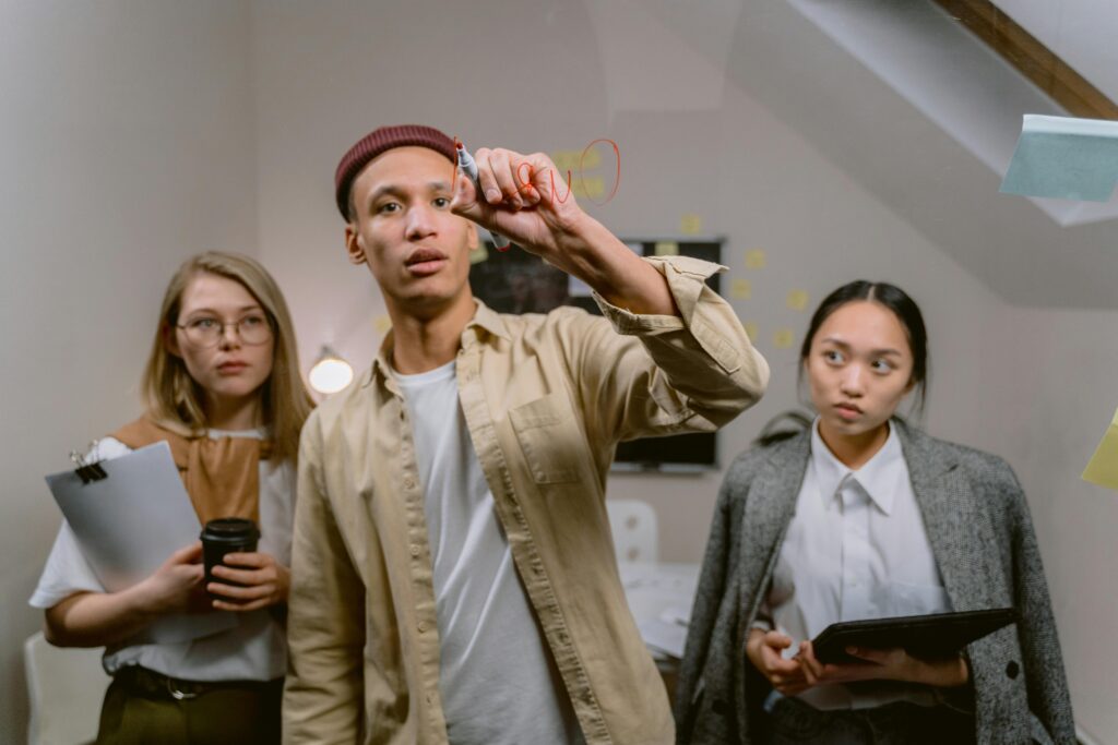 Three diverse young professionals brainstorming ideas on glass board in modern office setting.