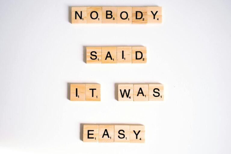 Close-up of wooden Scrabble tiles spelling 'nobody said it was easy' on a white background.